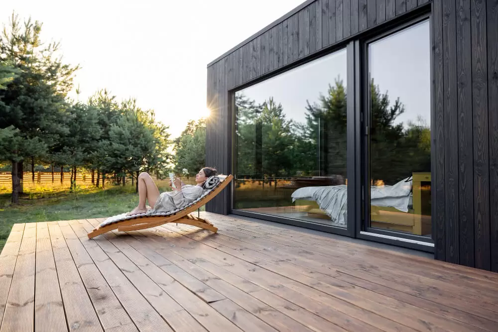 Large black aluminum sliding glass door opening to wooden deck with garden view